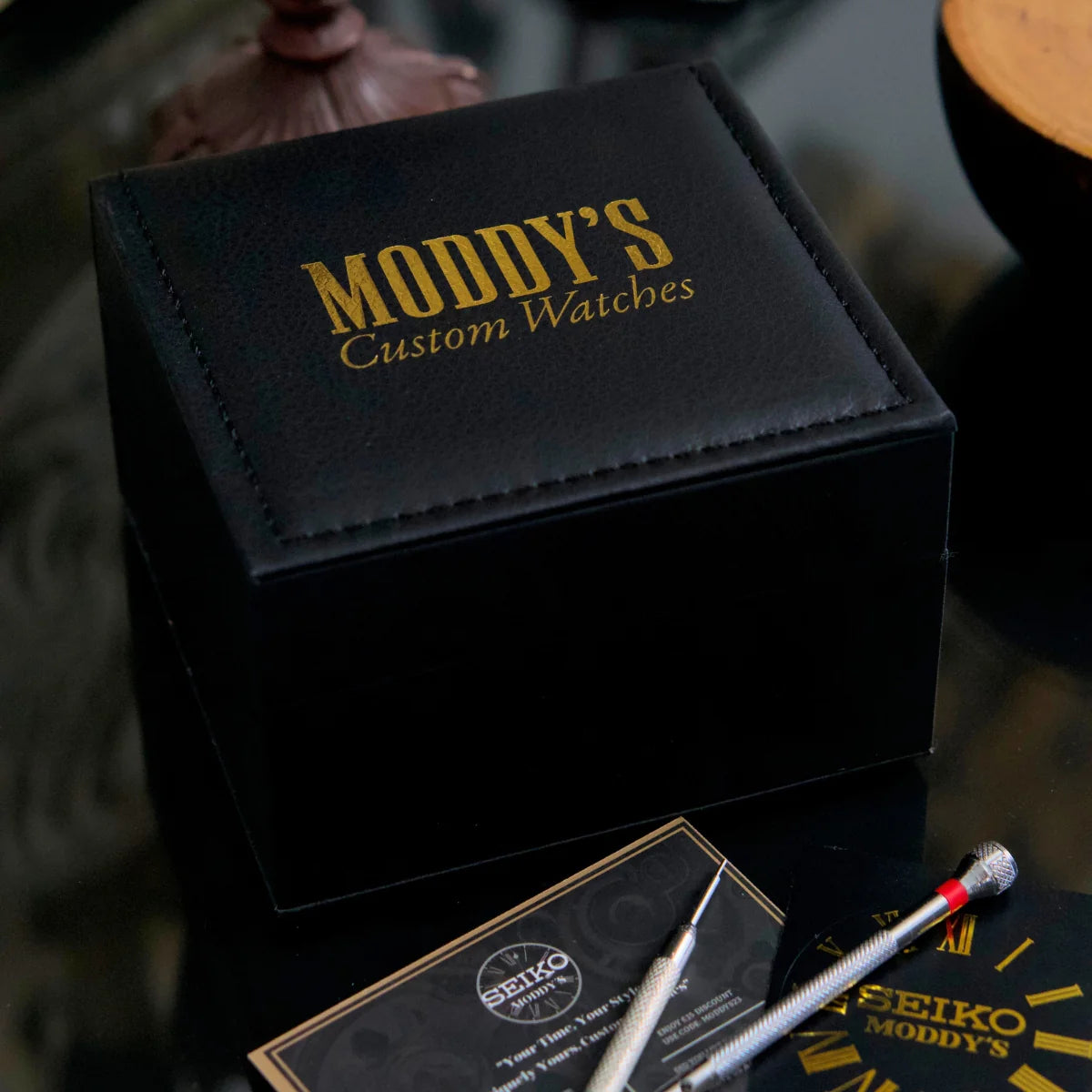 Black watch box with 'Moddy's Custom Watches' branding on a reflective surface.